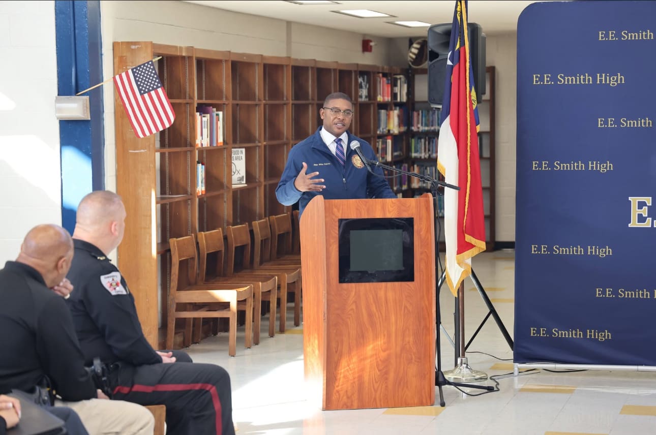 Man speaking at high school podium with officers